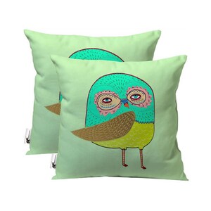 May include: Two green throw pillows with a colorful owl design. The owl has large eyes, a yellow beak, and brown wings.