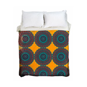 May include: A bed with white pillows and a duvet cover featuring a repeating mandala pattern. The mandala design has teal, red, and purple accents on a yellow background. The bedding is neatly arranged.