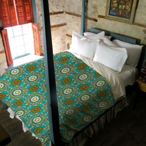 Puede incluir: Un edred&oacute;n estampado en turquesa y amarillo con un volante blanco. El edred&oacute;n est&aacute; sobre una cama con almohadas blancas y una cabecera de madera.