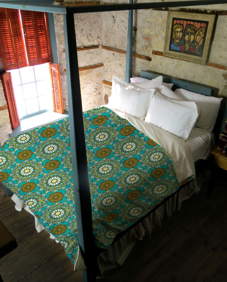 Puede incluir: Un edred&oacute;n estampado en turquesa y amarillo con un volante blanco. El edred&oacute;n est&aacute; sobre una cama con almohadas blancas y una cabecera de madera.