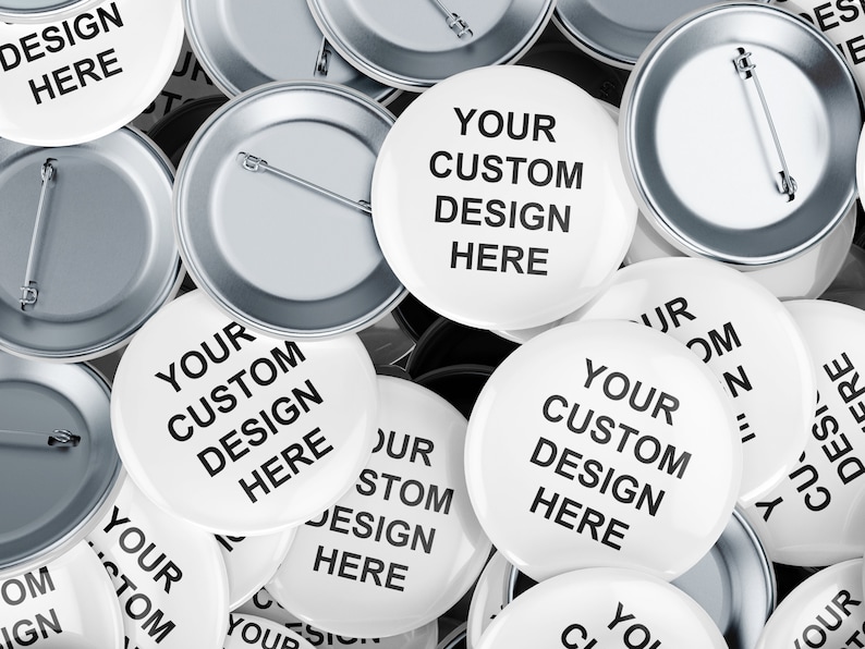 Puede incluir: Un mont&oacute;n de botones redondos blancos con respaldos plateados. Los botones tienen el texto "Your Custom Design Here" impreso en ellos.