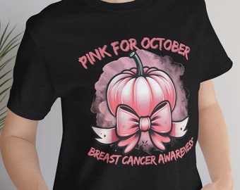 Op de afbeelding: Zwart T-shirt met een roze pompoenafbeelding en de tekst "PINK FOR OCTOBER BREAST CANCER AWARENESS". De pompoen heeft een strik en is omgeven door een roze aquareleffect.
