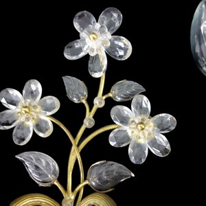 Pu&ograve; includere: Applique da parete in metallo dorato con fiori e foglie in vetro trasparente. L'applique ha una singola lampadina.