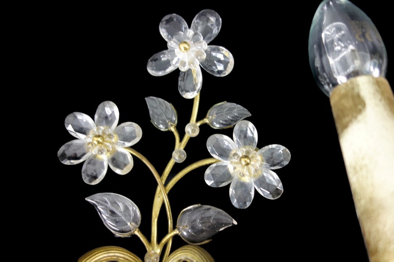 Pu&ograve; includere: Applique da parete in metallo dorato con fiori e foglie in vetro trasparente. L'applique ha una singola lampadina.