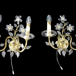 Pu&ograve; includere: Un paio di applique da parete dorate con fiori e foglie in vetro trasparente. Ogni applique ha due lampadine a forma di candela.