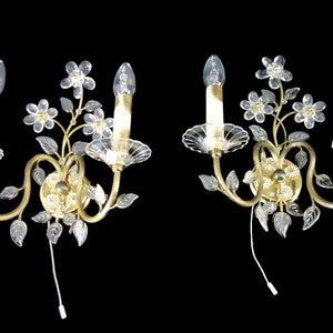 Pu&ograve; includere: Un paio di applique da parete dorate con fiori e foglie in vetro trasparente. Ogni applique ha due lampadine a forma di candela.