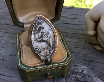 May include: A silver ring with a cameo of a woman holding a fan. The cameo is set in an oval-shaped frame and is surrounded by a gold band. The ring is in a green velvet box.