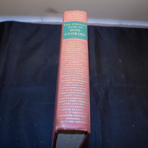 May include: The Fireside Book of Dog Stories, a red hardcover book with a green spine listing the authors of the stories included. The authors include Jack London, Thomas Mann, and more.
