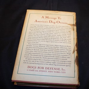 May include: A vintage book cover with a message to America's dog owners. The cover is cream colored with brown text. The title is "A Message To America's Dog-Owners". The text explains the need for dogs in the war effort and encourages dog owners to register their dogs for service.
