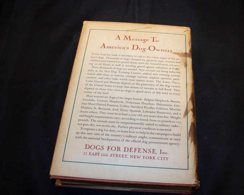May include: A vintage book cover with a message to America's dog owners. The cover is cream colored with brown text. The title is "A Message To America's Dog-Owners". The text explains the need for dogs in the war effort and encourages dog owners to register their dogs for service.