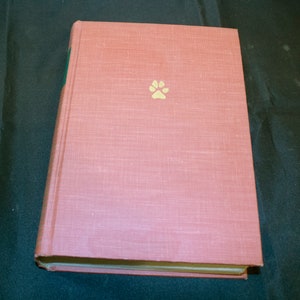 May include: A pink hardcover book with a gold paw print on the front cover.