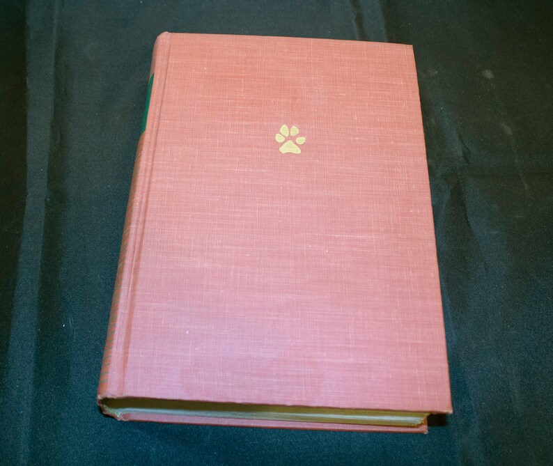May include: A pink hardcover book with a gold paw print on the front cover.
