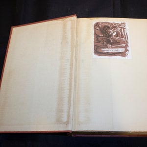 May include: An open book with a brown illustration of a person working on a book with the text "Marvil F. Dudley" on the illustration.