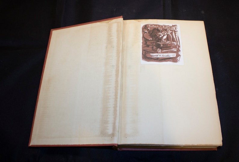 May include: An open book with a brown illustration of a person working on a book with the text "Marvil F. Dudley" on the illustration.