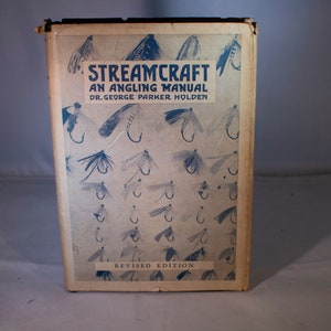 May include: A vintage book titled "Streamcraft: An Angling Manual" by Dr. George Parker Holden. The cover features a pattern of various fishing flies with hooks, and the text "Revised Edition" is printed at the bottom.