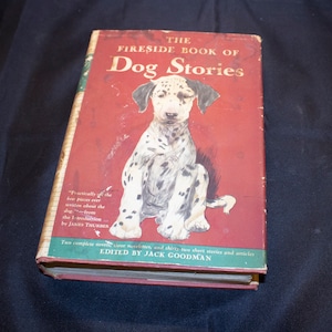 May include: The Fireside Book of Dog Stories, a red hardcover book with a black and white illustration of a Dalmatian puppy on the front cover. The book title is in white text and the author's name is in black text.