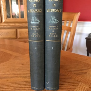 May include: Two vintage books titled "America in Midpassage" by Charles A. Beard and Mary R. Beard. The books are dark blue with gold lettering and a ship illustration. The publisher is Macmillan. Volume II and Volume I are visible.
