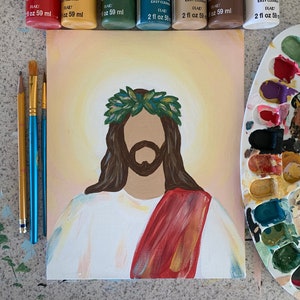 May include: A painting of Jesus Christ on a canvas with a red robe and a crown of thorns. The painting is surrounded by paint tubes and a paint palette.