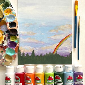May include: A set of ten 2-ounce bottles of acrylic paint in various colors, including snow white, bright red, pumpkin orange, cinder gold, lime this, marsh green, blue cotton, and velvet crush. The bottles are arranged in a row on a white surface. The paint is labeled "Apple Barrel" and is suitable for crafting and painting.