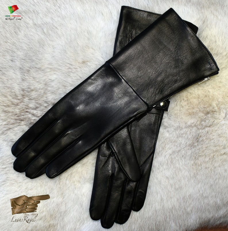 May include: A pair of black leather gloves with a zipper on the cuff. The gloves are laid out on a white furry surface.