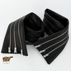 May include: Black leather belt with multiple zipper details. The belt is folded in half and the zippers are visible on both sides.