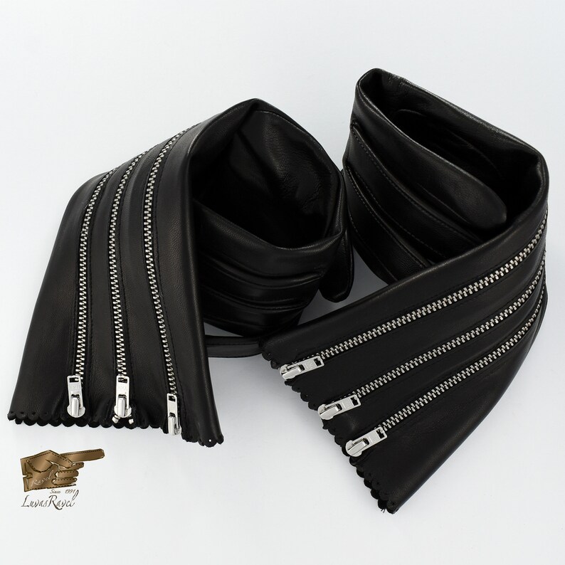 May include: Black leather belt with multiple zipper details. The belt is folded in half and the zippers are visible on both sides.