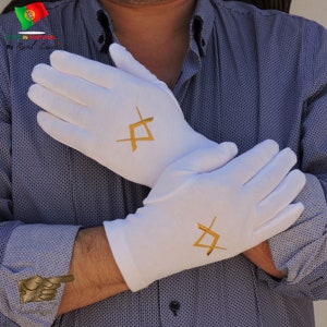 May include: A pair of white cotton gloves with gold embroidery of a square and compass symbol. The gloves are worn by a person with a blue patterned shirt.