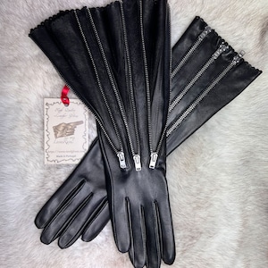 May include: A pair of black leather gloves with multiple zippers up the back of the hand. The gloves have a scalloped edge at the wrist. The gloves are made in Portugal.