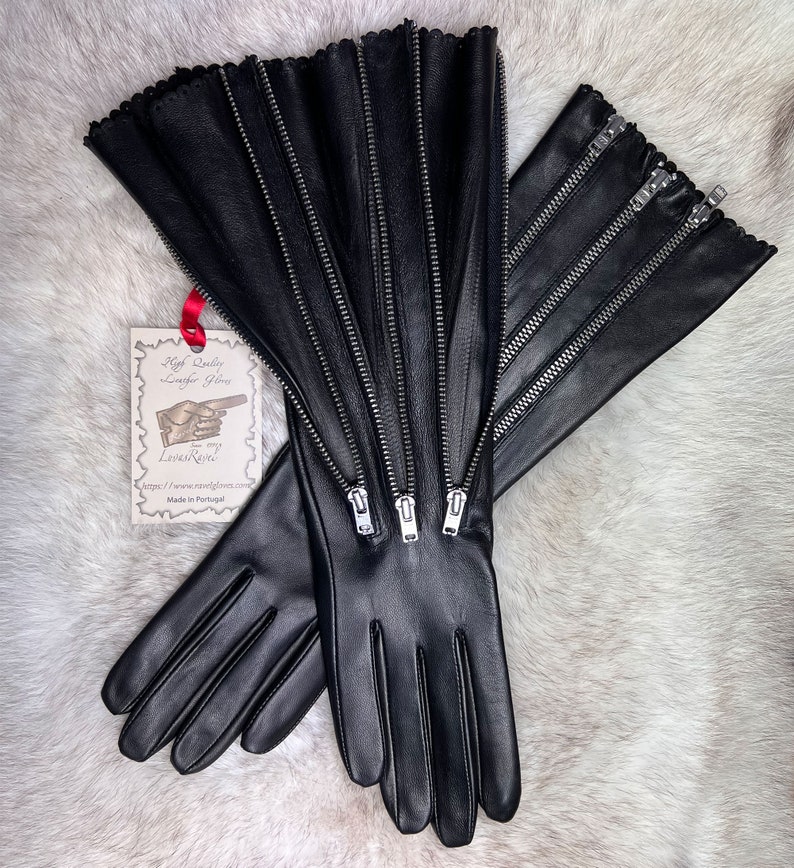 May include: A pair of black leather gloves with multiple zippers up the back of the hand. The gloves have a scalloped edge at the wrist. The gloves are made in Portugal.