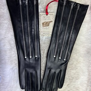 May include: A pair of long black leather gloves with four silver zippers on each glove. The gloves have a ruffled edge and are made in Portugal.
