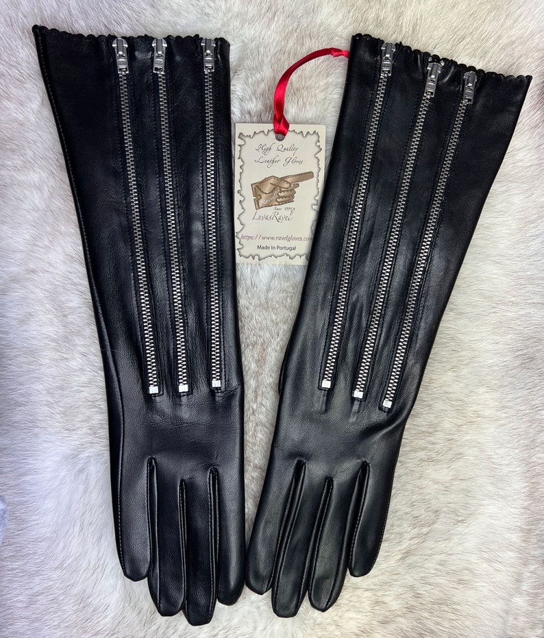May include: A pair of long black leather gloves with four silver zippers on each glove. The gloves have a ruffled edge and are made in Portugal.