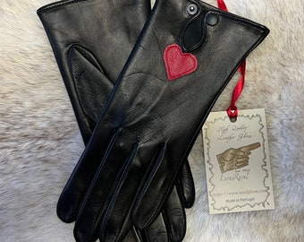 May include: Black leather gloves with a red heart detail. The gloves are folded in half and a tag is attached to the wrist of one glove. The tag reads "High Quality Leather Gloves" and "Luisa Reyes".