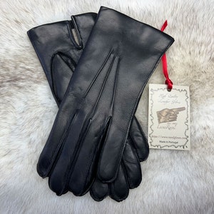 Könnte beinhalten: Ein Paar schwarze Lederhandschuhe mit einem roten Band und einem Etikett mit der Aufschrift "High Quality Leather Gloves, Levai Ravel, https://www.levairavelgloves.com, Made in Portugal".