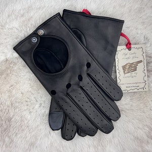 Pode incluir: Luvas de condução de couro preto com detalhes perfurados e um grande furo na parte de trás da mão. As luvas estão dobradas e colocadas sobre uma superfície de pele branca. Uma etiqueta com o texto "High Quality Leather Gloves" é visível no fundo.