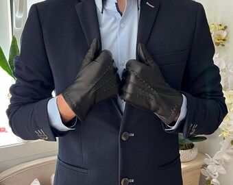 Peut inclure: Gants en cuir noir avec coutures décoratives portés avec un blazer bleu marine et une chemise bleu clair. Les gants ont un design classique et semblent être en cuir de haute qualité.