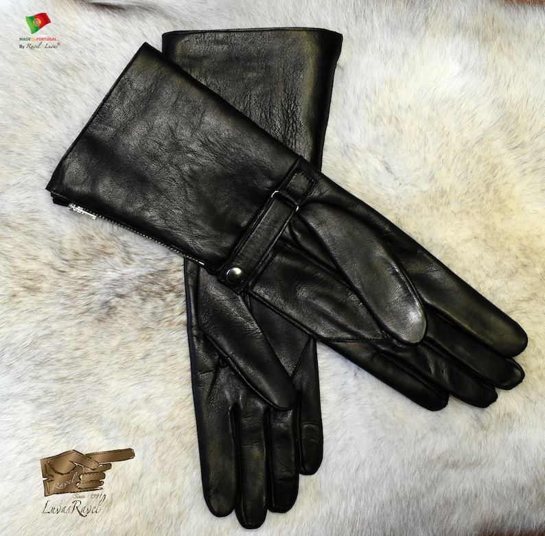 May include: A pair of black leather gloves with a long cuff and a strap with a buckle. The gloves have a zipper on the cuff and are made in Portugal.