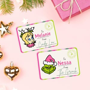 Könnte beinhalten: Zwei rechteckige Geschenkanhänger mit Zeichentrickfiguren. Einer zeigt Cindy Lou Who, der andere den Grinch. Beide Anhänger tragen Namen und die Worte "North Pole Express Mail". Die Anhänger befinden sich auf einem rosa Hintergrund.
