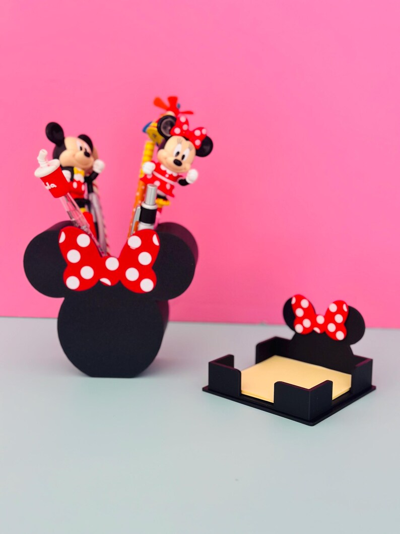 Puede incluir: Juego de organizadores de escritorio negros con tem&aacute;tica de Minnie Mouse. Incluye un portal&aacute;pices con forma de cabeza de Minnie con un lazo de lunares rojos y blancos, y un portanotas. Bol&iacute;grafos con figuras de Minnie Mouse est&aacute;n en el portal&aacute;pices.