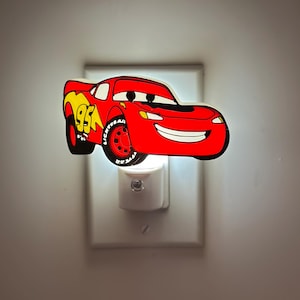 May include: A red and yellow Lightning McQueen night light. The night light is shaped like the animated race car with the number 95 on the side. The night light plugs into a standard wall outlet.
