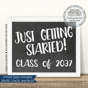May include: A black chalkboard with white text that reads "Just Getting Started! Class of 2037". The chalkboard is framed in white and has a white background.