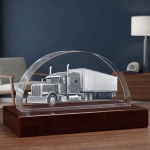 Op de afbeelding: Een model van een vrachtwagen met een gedetailleerde zilveren cabine en een lange witte trailer, ingesloten in een doorzichtige, boogvormige acryl displaykap. Het geheel is gemonteerd op een massieve, rechthoekige donkerbruine houten voet.