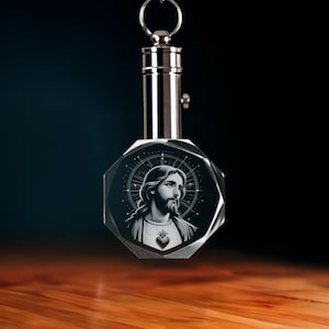 May include: A crystal keychain featuring a portrait of Jesus Christ. The image is encased in a faceted, octagonal crystal with a silver-colored metal top and keyring. The portrait is in black and white, with a halo effect.