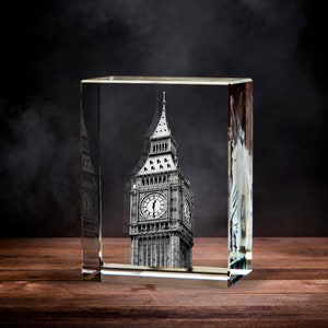 May include: A clear glass cube with a black and white image of Big Ben inside. The cube is sitting on a wooden surface.