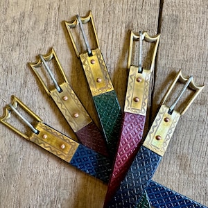 May include: Five leather belts with brass buckles. The belts are in different colors, including green, red, and blue. The buckles have intricate designs.