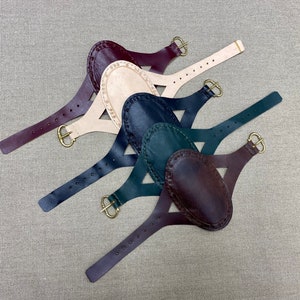 Könnte beinhalten: Fünf Lederarmbänder mit ovalen Lederflicken. Die Armbänder sind in verschiedenen Farben, darunter Burgunderrot, Beige, Dunkelblau, Grün und Braun. Jedes Armband hat eine Messing-Schnalle.