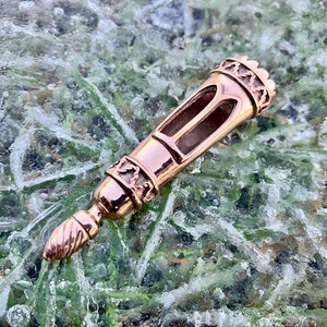 May include: A rose gold metal bottle stopper with an intricate design. The stopper has a pointed tip and a decorative top with a crown-like design.