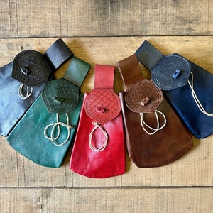 Puede incluir: Cinco bolsas de cuero con cordones de ajuste y cierres de solapa decorativos. Las bolsas son de varios colores, incluyendo azul, verde, rojo, marrón y negro.