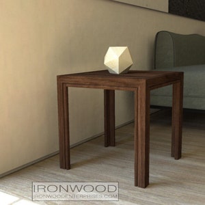 Puede incluir: Una mesa auxiliar de madera marrón oscuro con una tapa cuadrada y cuatro patas. Un objeto geométrico blanco se encuentra sobre la tapa de la mesa.