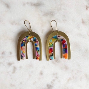 May include: A pair of gold arch-shaped earrings with colorful, multi-colored, confetti-like resin inserts.