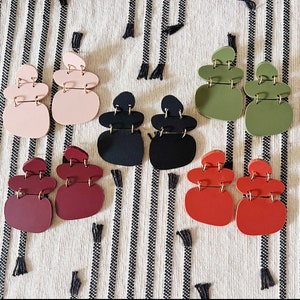 Op de afbeelding: Zes paar statement oorbellen met een gestapelde, abstracte vormgeving. De oorbellen zijn gemaakt van polymer clay en zijn verkrijgbaar in verschillende kleuren, waaronder zwart, rood, groen en roze.